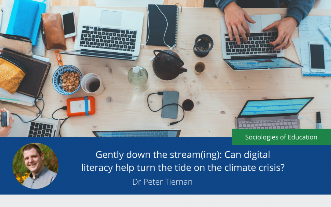 Image with headline 'Gently down the stream(ing): Can digital literacy help turn the tide on the climate crisis?' over a photo of a wooden table. On the table are various devices, such as laptops, and mobile phones. The hands of one person can be seen as they type on one of the laptops.